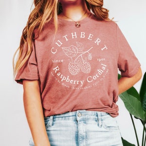 May include: A pink t-shirt with a white graphic design that says "CUTHBERT since 1901 Raspberry Cordial not to be drunk three tumbler fulls at a time".