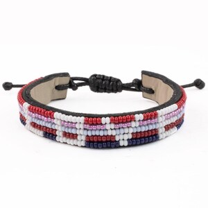 May include: A beaded bracelet with a black leather backing and adjustable black cord closure. The bracelet features rows of red, white, pink, and blue beads. The bracelet is approximately 0.75 inches wide.