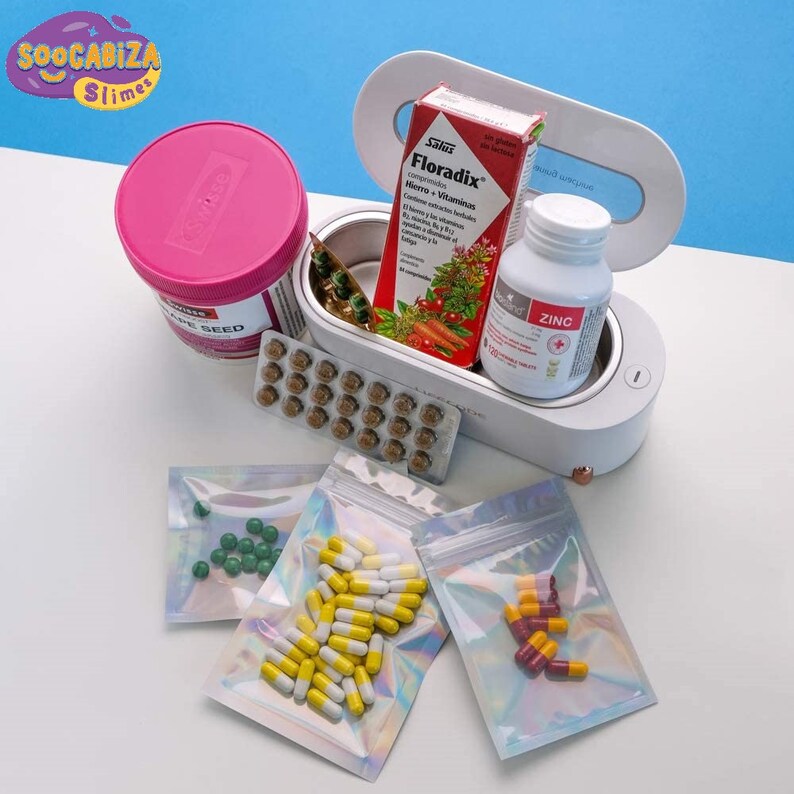 K&ouml;nnte beinhalten: Ein wei&szlig;er Pillenorganizer mit einem durchsichtigen Deckel, der verschiedene Pillen und Kapseln enth&auml;lt. Der Organizer ist ge&ouml;ffnet und hat einen kleinen Knopf an der Seite. Es gibt auch mehrere kleine Plastikt&uuml;ten, die mit Pillen und Kapseln gef&uuml;llt sind.