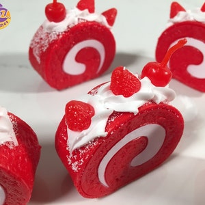 May include: Four red and white swirl cake rolls with white frosting and red cherries on top.  The cake rolls are decorated with red sprinkles and white powdered sugar.  The cake rolls are on a white surface.  Soocabiza Slimes.