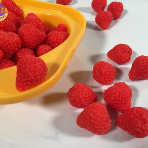 May include: A yellow bowl filled with red, strawberry-shaped slime.  The bowl is tipped over, spilling the slime onto a white surface.  There are several red, strawberry-shaped slime pieces scattered on the surface.