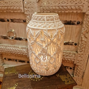 Può includere: Lanterna per candele in macramé bianco con perline di legno. La lanterna è appoggiata su una scatola di legno con dettagli in ottone.