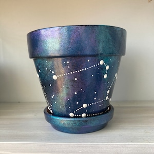 May include: A dark blue iridescent ceramic planter with a white constellation design. The planter has a matching saucer.