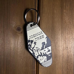 May include: A white and black motel key chain with the text "Joshua Tree" and a silhouette of Joshua Tree National Park.