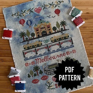 Op de afbeelding: Een kruissteekpatroon met een kleurrijke illustratie van een stadsscène met gebouwen, trams en de tekst "Melbourne, Australië". Het patroon is gedrukt op wit papier en bevat een zwart-witte ster met de tekst "PDF-PATROON".