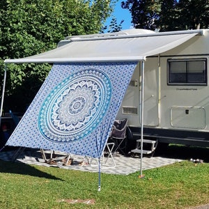 May include: A white camper van with an awning extended over a blue and white mandala tapestry. The tapestry is hanging from the awning and is covering a portion of the van. The van has the text "Campingemotions" on the side.