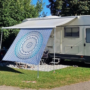 Könnte beinhalten: Ein weißer Wohnwagen mit einer Markise, die über eine blaue und weiße Mandala-Muster-Tapete gespannt ist. Die Markise wird von einem weißen Metallrahmen getragen. Der Wohnwagen hat eine weiße Tür mit dem aufgedruckten Text "Camping Emotions".