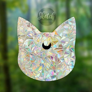 Könnte beinhalten: Ein katzenförmiger Sonnenfänger-Aufkleber mit einem holografischen Scherbenmuster, das Regenbogenfarben reflektiert. In der Mitte des Katzenkopfes befindet sich ein schwarzes Mondsichel-Symbol. Der Text Sketch YOUR WORLD ist oben zu sehen.