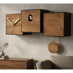 May include: A wall-mounted cuckoo clock featuring three connected wooden square boxes with black frames. The left box displays clock hands, the center box has a small arched opening with a white bird figure, and the right box has a round wooden pendulum.