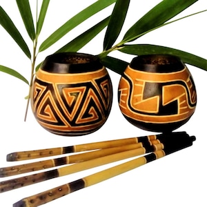 Puede incluir: Dos calabazas marrones con diseños geométricos negros y naranjas, utilizadas para beber mate, con cuatro pajitas de bambú.