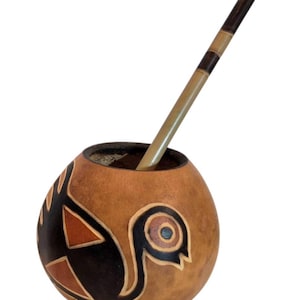 Può includere: Una tazza di mate a forma di zucca marrone con un motivo decorativo di uccello in nero, arancione e crema. Una cannuccia di legno, o bombilla, è inserita nella tazza. La zucca è alta circa 10 cm.