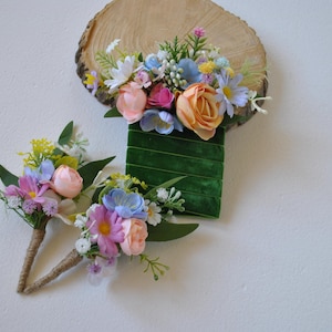 Op de afbeelding: Twee kleine bloemstukken met pastelroze, blauwe en gele bloemen. De arrangementen zijn op een witte achtergrond en zijn perfect voor een bruiloft of speciale gelegenheid.