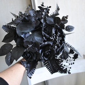 May include: A black wedding bouquet with roses, orchids, and ferns. The bouquet is tied with a black ribbon.