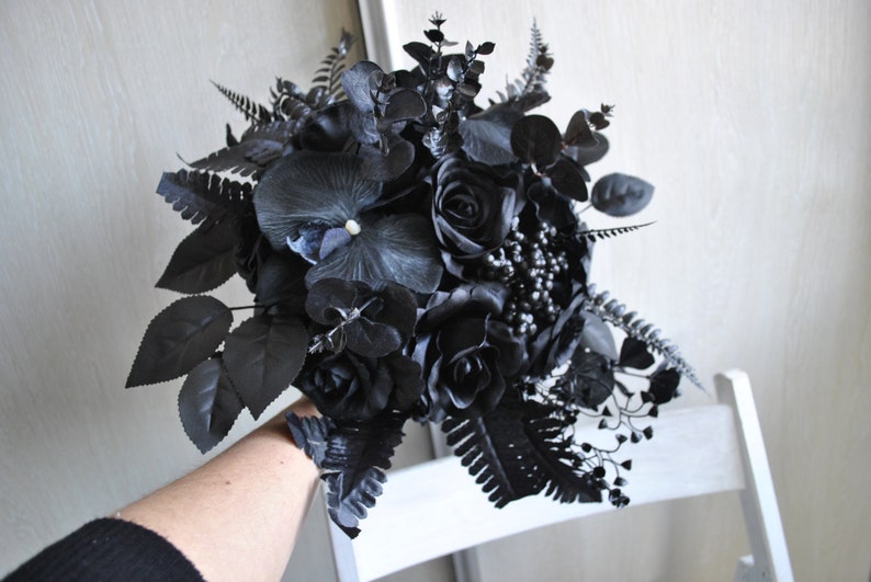 May include: A black wedding bouquet with roses, orchids, and ferns. The bouquet is tied with a black ribbon.