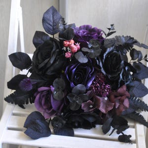 May include: A dark purple and black bridal bouquet with roses, ferns, and other foliage.