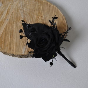 May include: A single black rose with green leaves and stems, arranged in a bouquet. The bouquet is displayed on a wooden slice.