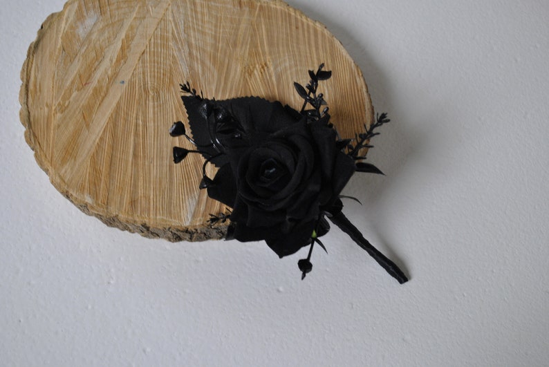 May include: A single black rose with green leaves and stems, arranged in a bouquet. The bouquet is displayed on a wooden slice.
