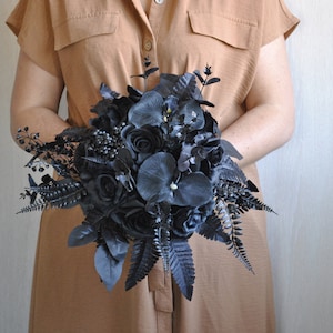 May include: A black wedding bouquet with roses, ferns, and other foliage.