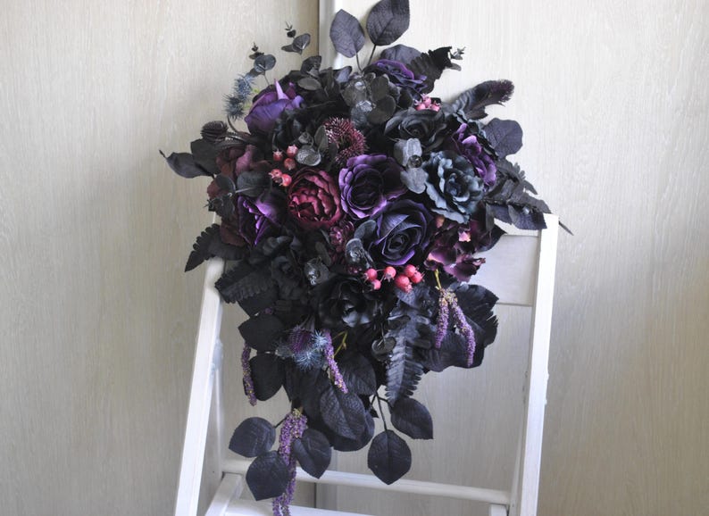 May include: A cascading bouquet of dark purple and black silk flowers with green leaves. The bouquet is arranged in a teardrop shape and is perfect for a gothic wedding or event.