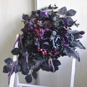 May include: A dark purple and black bridal bouquet with roses, ferns, and other greenery.