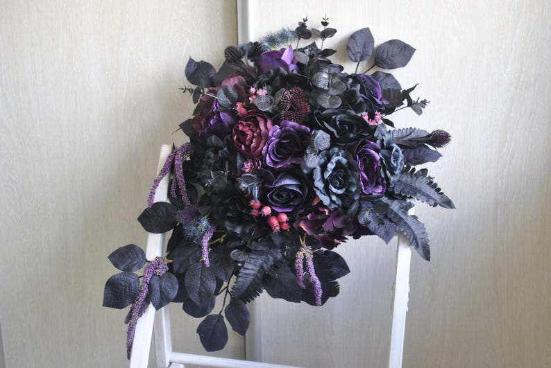 May include: A dark purple and black bridal bouquet with roses, ferns, and other greenery.