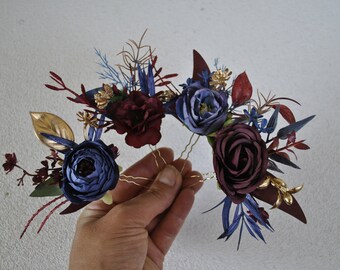 May include: Burgundy and blue floral hair comb with gold accents. The comb is made of artificial flowers and leaves and is attached to a gold wire hairpin.