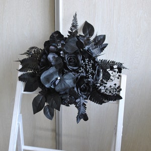 May include: A black wedding bouquet with black roses, orchids, and ferns.