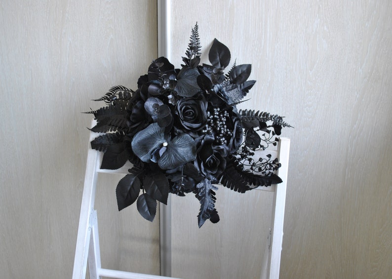 May include: A black wedding bouquet with black roses, orchids, and ferns.
