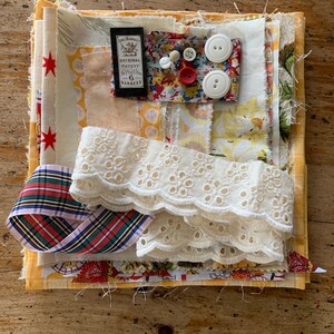 May include: A collection of fabric scraps, lace, ribbon, buttons, and a vintage sewing notions box. The fabrics are in various colours and patterns, including red, white, yellow, and blue. The lace is white and delicate. The ribbon is plaid and red, white, and blue. The buttons are white and have a floral design. The sewing notions box is brown and has the text "Original Patent No. Plus the 6 Harness" on it.