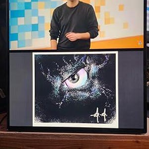 Peut inclure: Un écran d'ordinateur affiche deux images. L'image du haut montre une personne portant des lunettes et un pull noir devant un fond coloré. L'image du bas est une impression carrée d'un œil sur fond sombre, avec la signature de l'artiste.