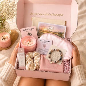 May include: A pink gift box containing a candle with crystals, a beaded bracelet, a satin sleep mask, a scrunchie, a small pouch, and informational cards. The box lid features the text Be your own kind of beautiful and a card reads Just for.