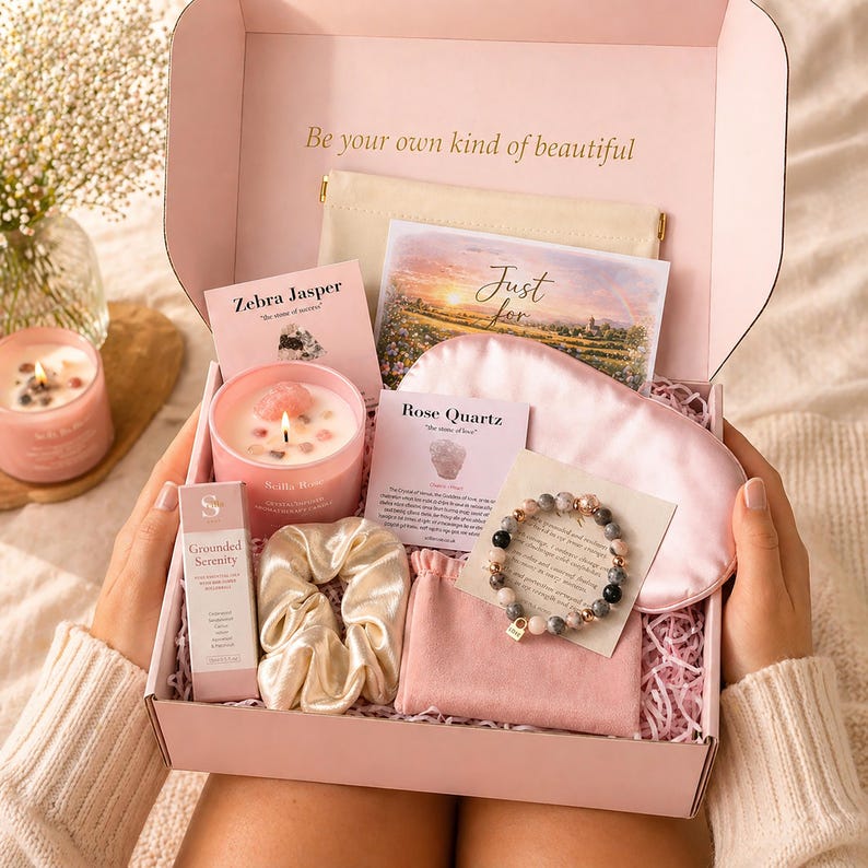 May include: A pink gift box containing a candle with crystals, a beaded bracelet, a satin sleep mask, a scrunchie, a small pouch, and informational cards. The box lid features the text Be your own kind of beautiful and a card reads Just for.