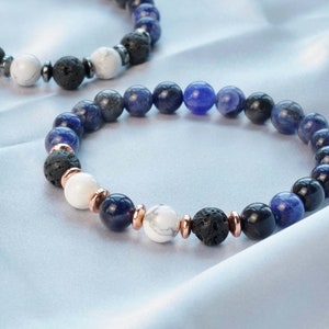 May include: Two bracelets featuring blue, white and black beads. The bracelets are made from lava rock, white howlite and blue sodalite beads. The beads are separated by small gold-coloured spacers.