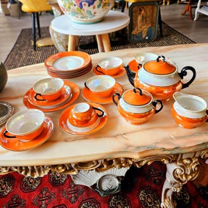 May include: A vintage tea set with orange and white porcelain cups, saucers, teapot, sugar bowl, and creamer. The set has black trim and a pearlescent finish.