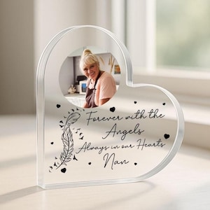 May include: A clear heart-shaped photo frame with a photo of a woman in the centre. The frame has the text "Forever with the Angels Always in our Hearts Nan" printed on it.