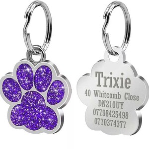 May include: Two silver dog tags with a paw print design. One tag has a purple glitter paw print and the other tag has the text "Trixie", "40 Whitcomb Close", "DN210UY", "07798425498", and "0770374377".