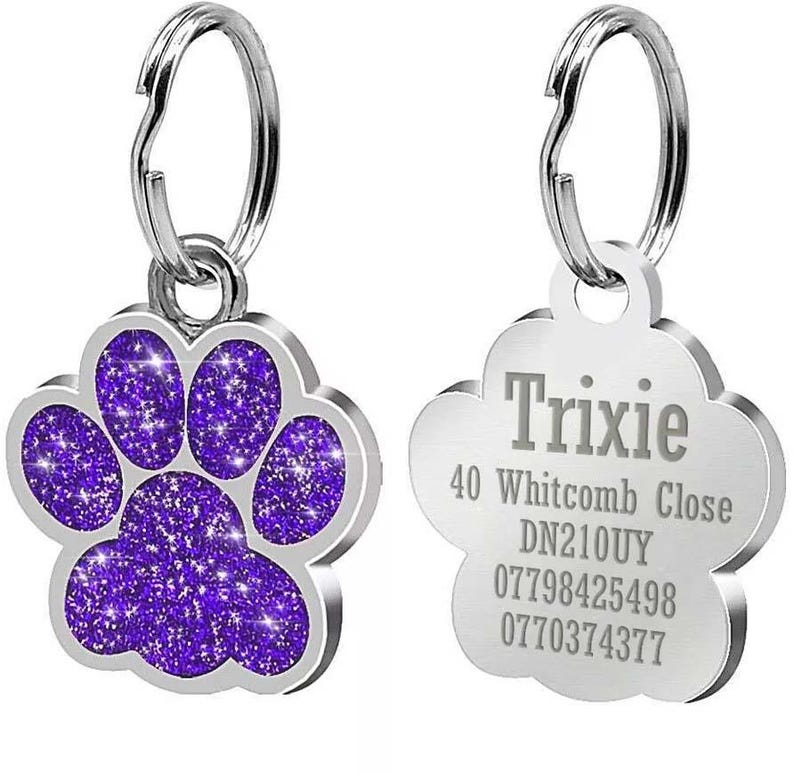 May include: Two silver dog tags with a paw print design. One tag has a purple glitter paw print and the other tag has the text "Trixie", "40 Whitcomb Close", "DN210UY", "07798425498", and "0770374377".