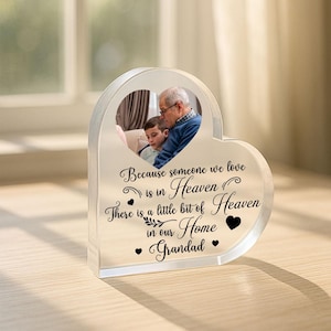 May include: A clear heart-shaped acrylic photo frame with a photo of a man and a boy. The frame has the text "Because someone we love is in Heaven There is a little bit of Heaven in our Home Grandad".