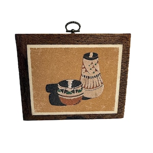 Puede incluir: Obra de arte enmarcada que presenta dos jarrones decorativos con diseños intrincados. La obra de arte está sobre un fondo beige y enmarcada en madera oscura texturizada. Un pequeño lazo de metal en la parte superior para colgar.