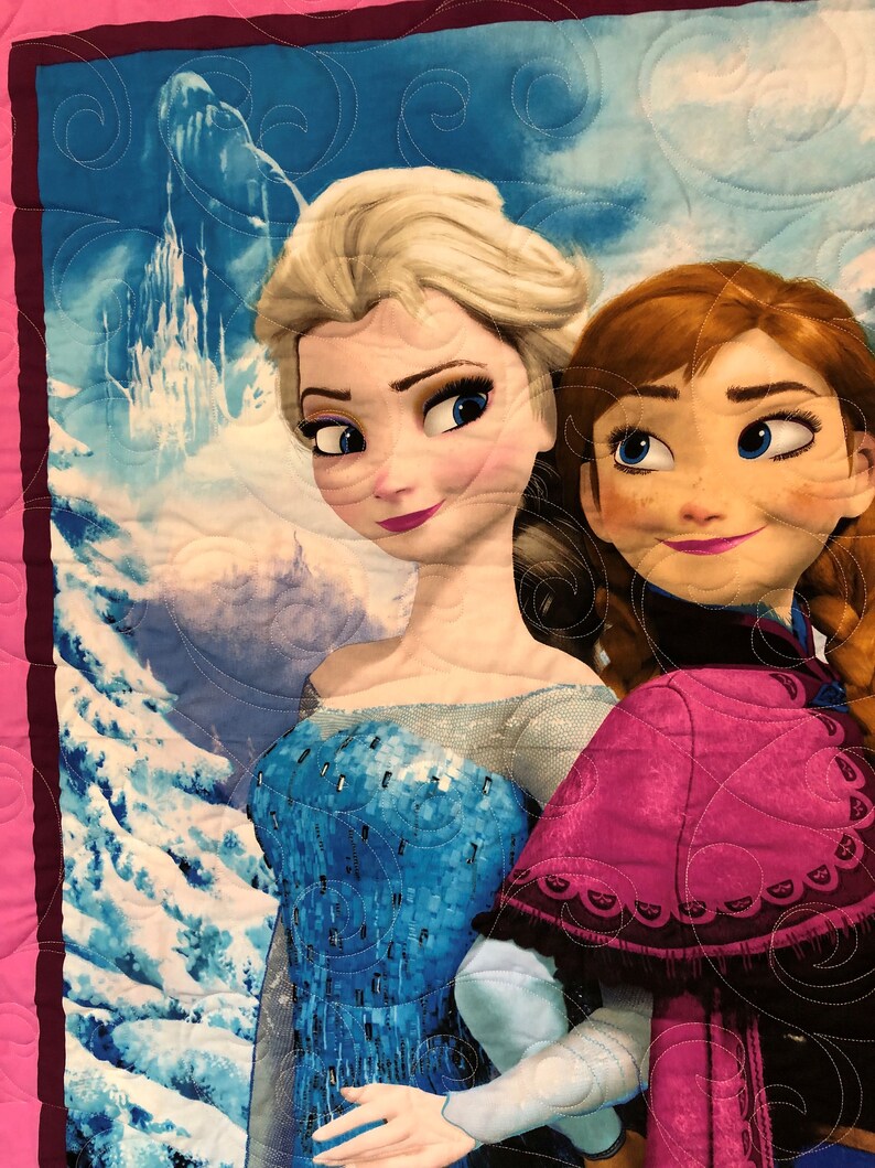Puede incluir: Dos chicas animadas, Elsa y Anna de la pel&iacute;cula Frozen, est&aacute;n de pie una al lado de la otra. Elsa lleva un vestido azul y plateado y Anna lleva un vestido rosa y morado. El fondo es una escena de monta&ntilde;a nevada.