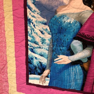 Puede incluir: Una manta acolchada rosa y amarilla con una imagen de una mujer con un vestido azul y un vestido rojo. La mujer con el vestido azul est&aacute; extendiendo una mano. El fondo es una escena de monta&ntilde;a nevada.