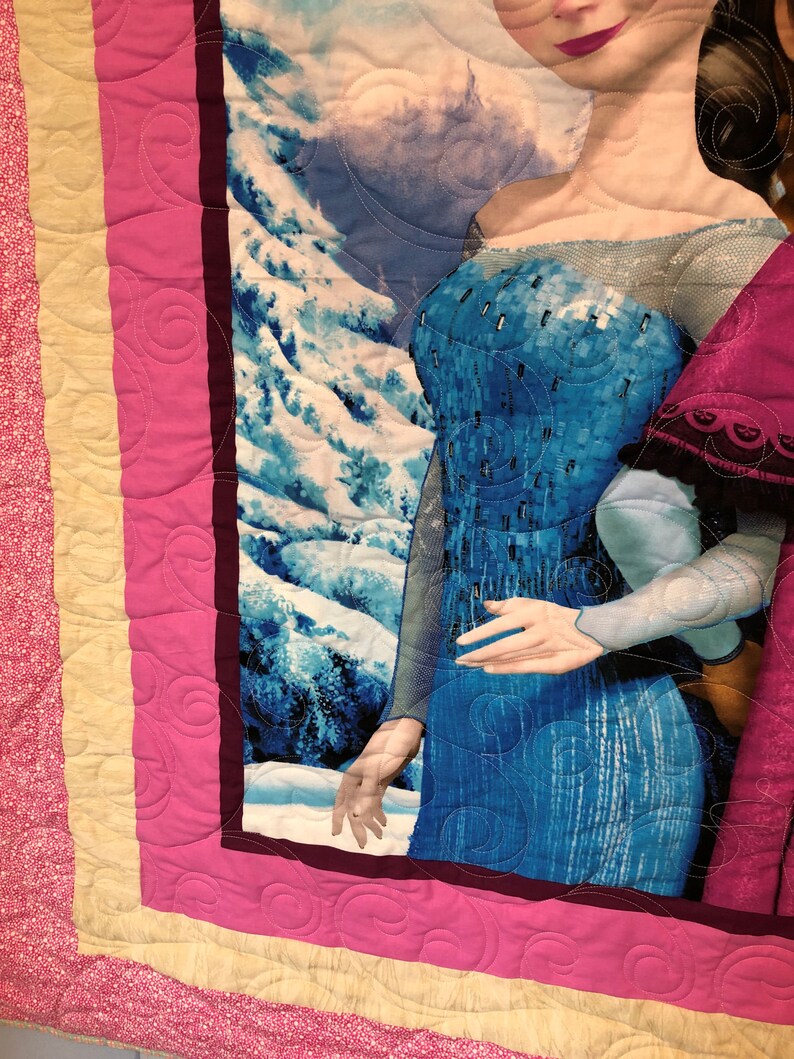 Puede incluir: Una manta acolchada rosa y amarilla con una imagen de una mujer con un vestido azul y un vestido rojo. La mujer con el vestido azul est&aacute; extendiendo una mano. El fondo es una escena de monta&ntilde;a nevada.
