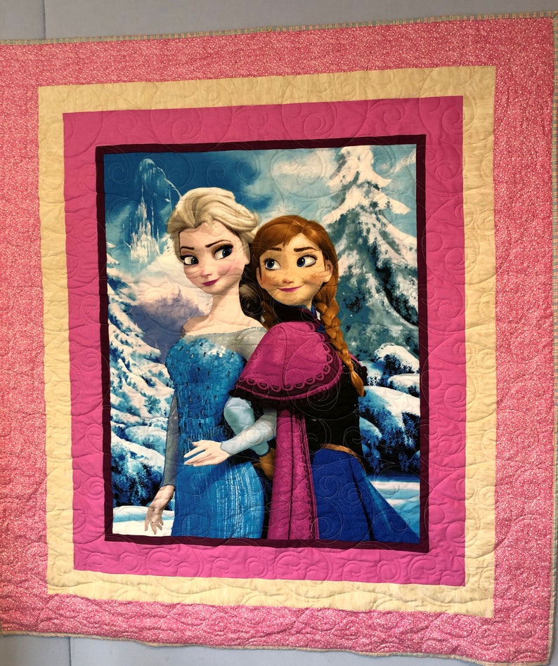 Puede incluir: Una manta acolchada rosa y amarilla con una imagen de Elsa y Anna de Frozen. La imagen muestra a las dos hermanas de pie juntas en un paisaje nevado.