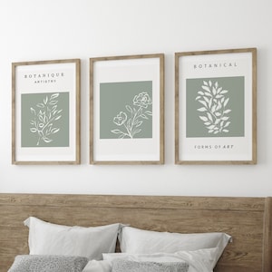 May include: A wooden bed frame with a white duvet and pillows. There are three framed prints above the bed with botanical illustrations and the text "BOTANIQUE ARTISTRY" and "BOTANICAL FORMS OF ART".