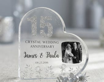 May include: Clear heart-shaped crystal photo frame with the number 15 in silver glitter, commemorating a crystal wedding anniversary. Includes a black and white photo and the names "James & Paula" with the date 08.23.2016.