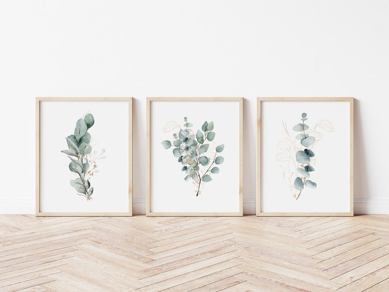 May include: Three framed prints with watercolor illustrations of eucalyptus branches with gold accents. The prints are displayed on a light wood floor.