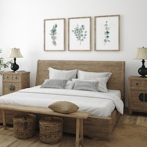 May include: A wooden bed frame with a white duvet and pillows, two bedside tables with lamps, and three framed botanical prints of eucalyptus leaves on the wall.