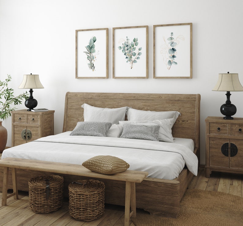 May include: A wooden bed frame with a white duvet and pillows, two bedside tables with lamps, and three framed botanical prints of eucalyptus leaves on the wall.