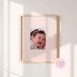 Puede incluir: Fotografía enmarcada de una niña sonriente con una diadema de lazo rosa. La fotografía está sobre un fondo rosa dentro de un marco de madera clara. Un círculo rosa con el texto "7 colores para elegir" está en la esquina inferior derecha.