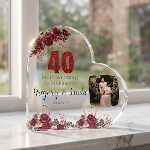 May include: A heart-shaped acrylic photo frame commemorating a 40th Ruby Wedding Anniversary. The frame features red floral accents, the number "40" in glitter, and the names "Gregory & Linda" with the date 03.05.1976. A photo of the couple is displayed.